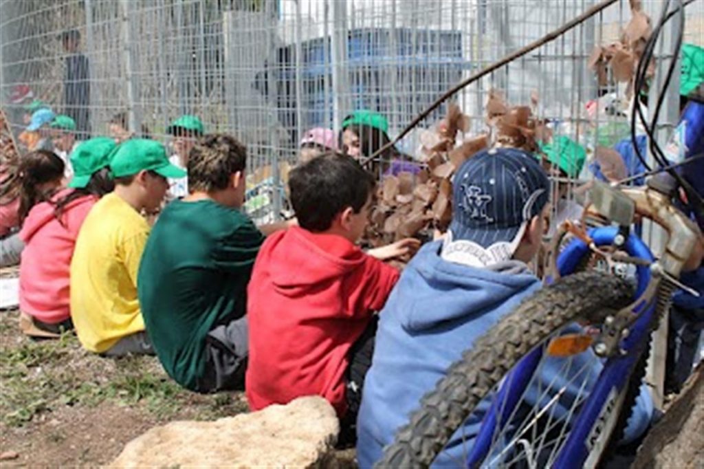 ילדי בת חפר בביצוע קשירת שקיות ניילון לגדר מרכז המיחזור