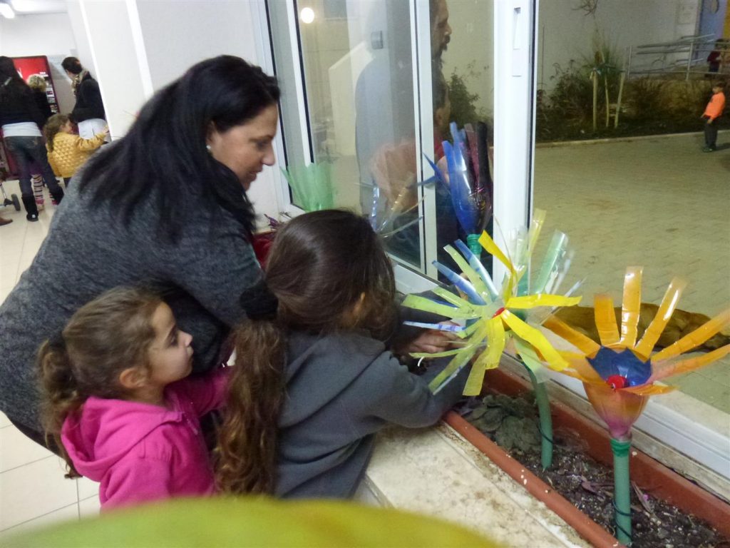 הילדים נהנים  לשתול את פרחי הבקבוקים באדניות המתנס